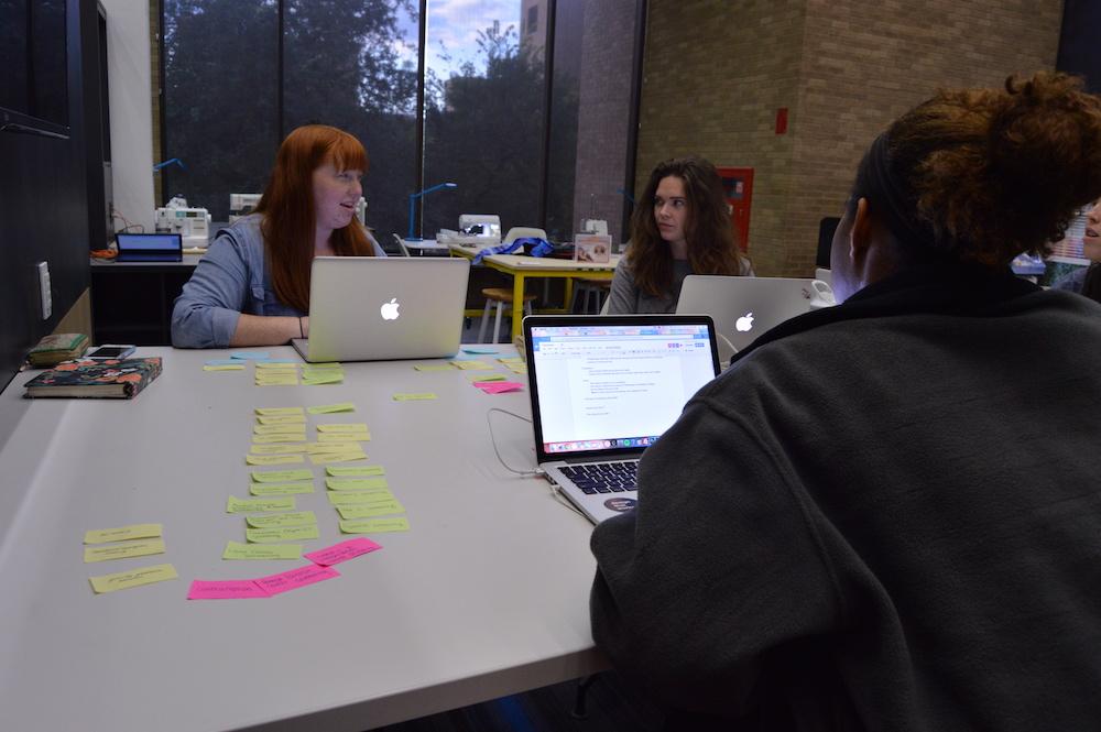 Three students work at a table covered in post-its