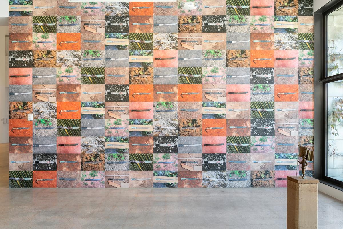 An installation of an artwork with a grid of photos of machetes against various backgrounds.