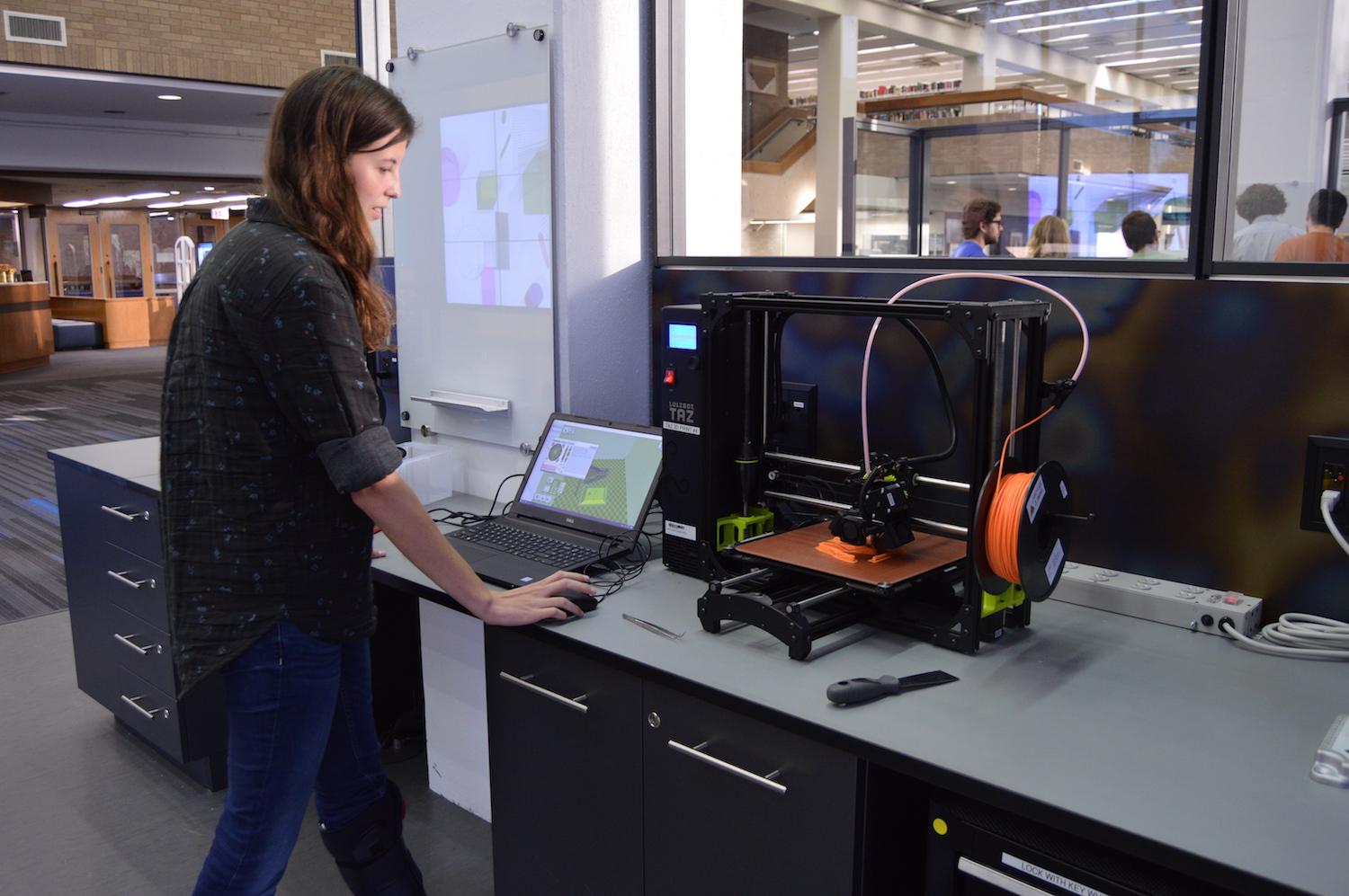 Alison stands at a laptop while she uses a 3D printer