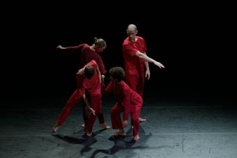 Four dancers in red jumpsuits perform on a stage