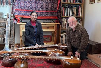 A graduate student sits next to a luthier, surrounded by sitar instruments.