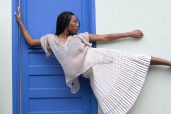 A dancer leans against the frame of a blue door, their left arm and leg extended parallel to the ground