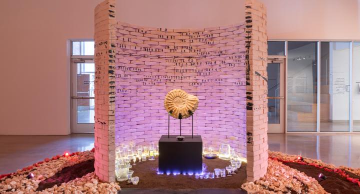 An alter with a shell fossil is at the center of a semi-circle brick wall in a museum gallery space