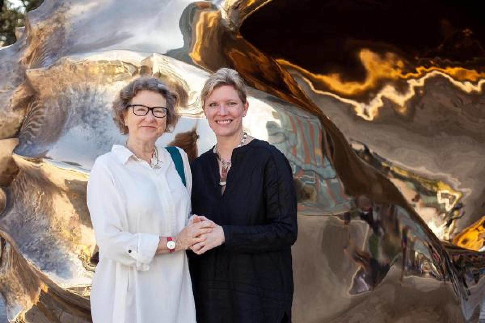 Two women posing in front of a painting