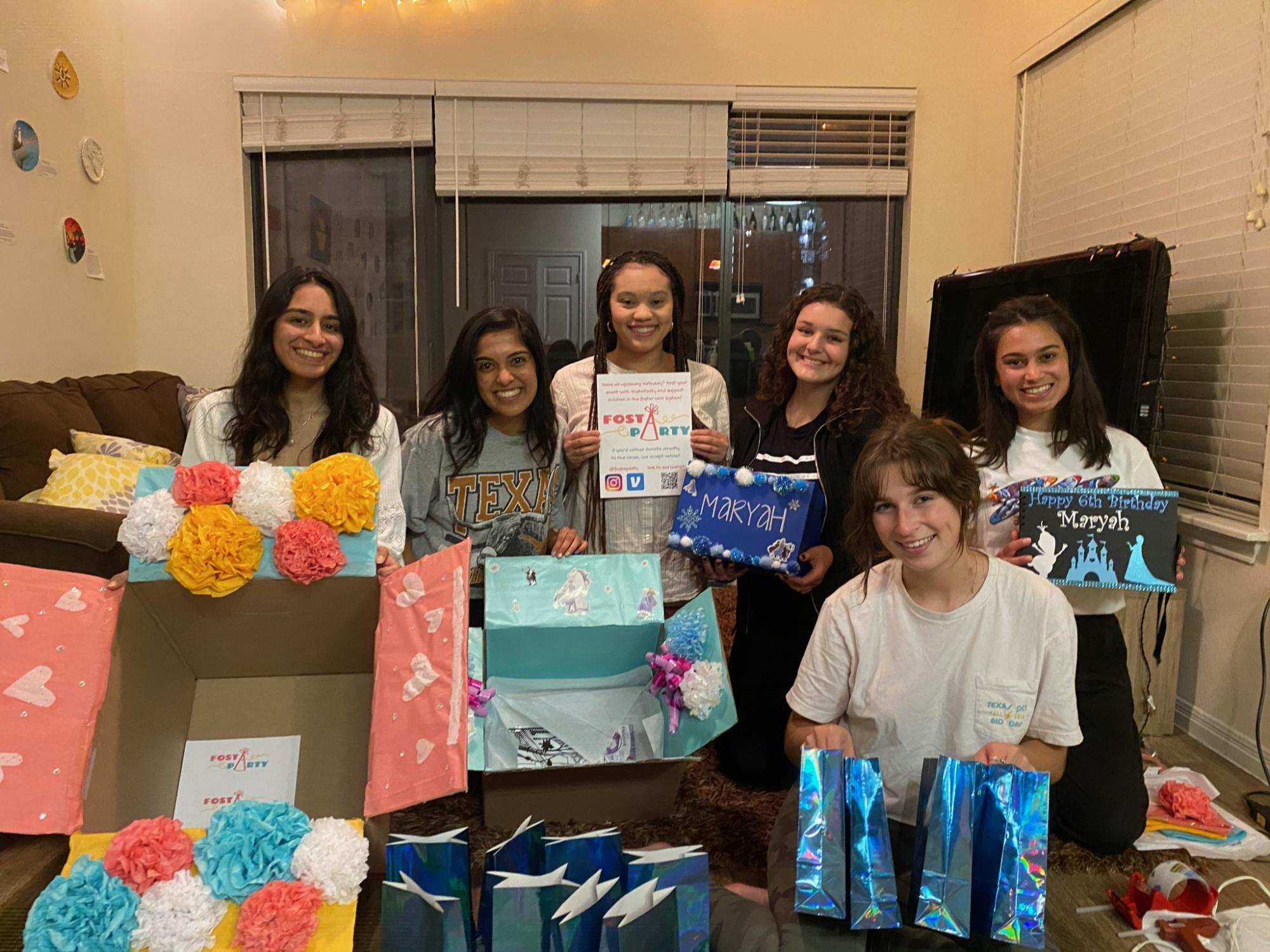 A group of six female college students pose with birthday party kits they created.