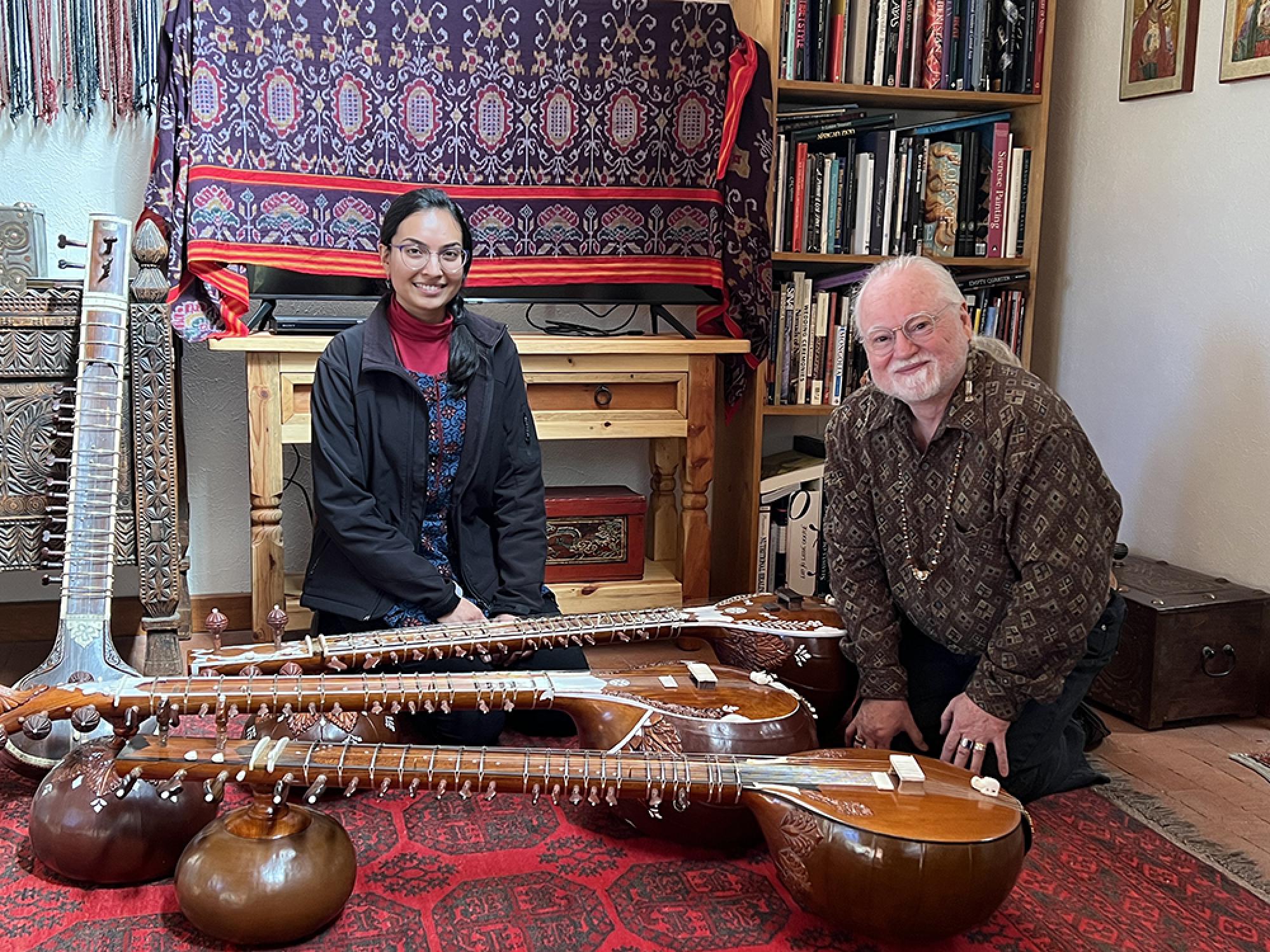 A graduate student sits next to a luthier, surrounded by sitar instruments.