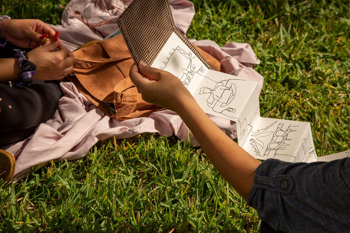 A student shows a portfolio of drawings on a lawn outside the art building. 
