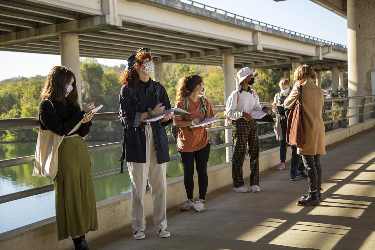 Students hold sketch books on a pedestrian bridge. 