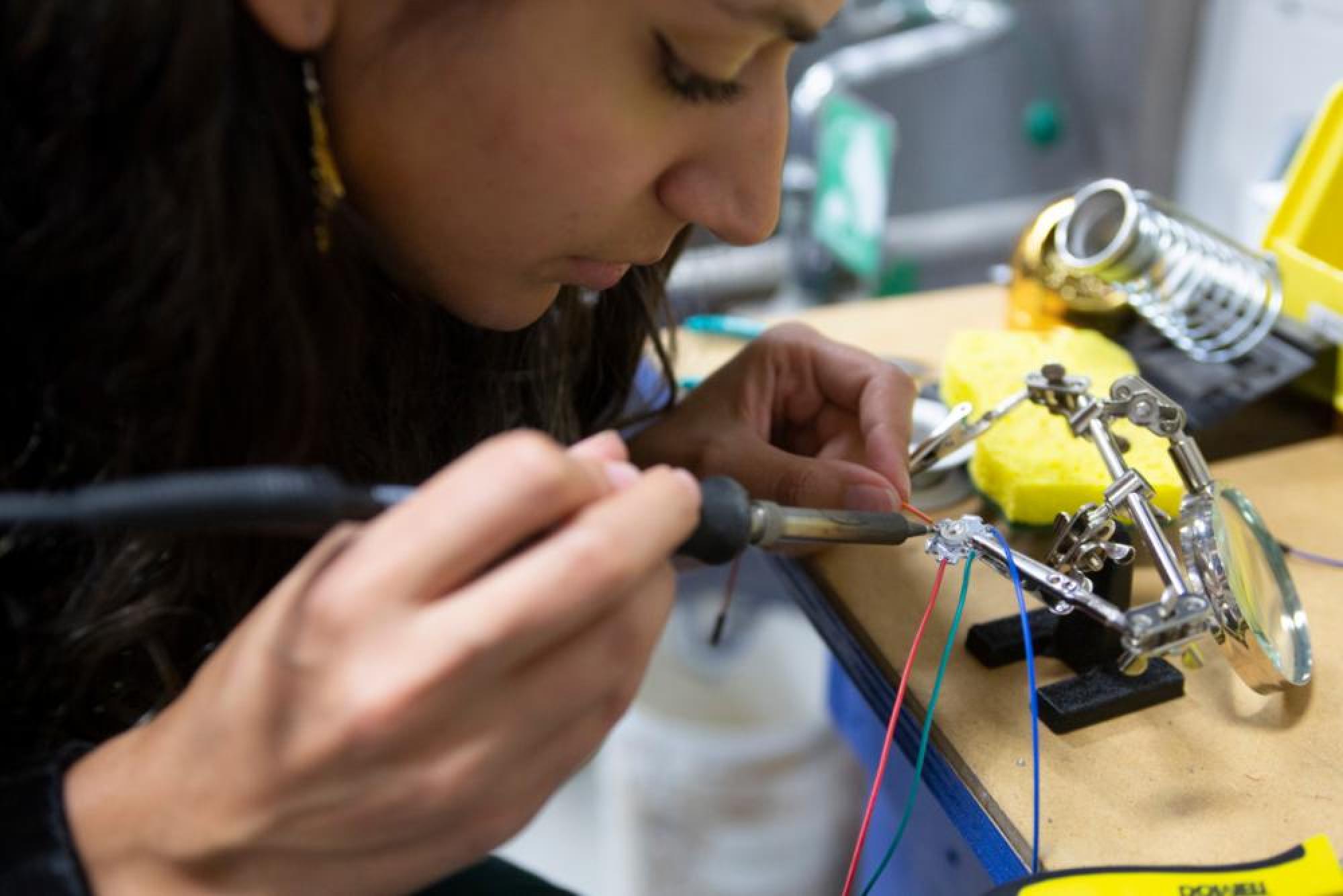 Adri Lara, an Arts and Entertainment Technologies senior, solders wiring as part of the lighting for the creek monster habitat.