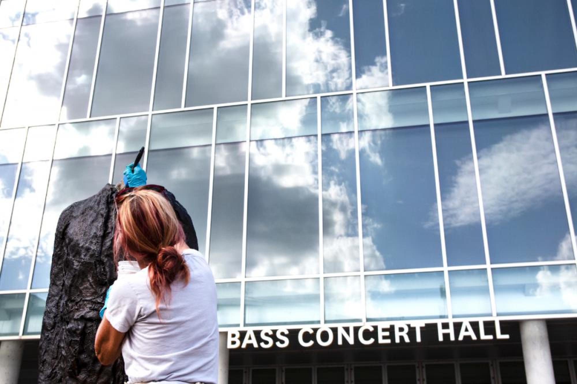 A conservationist from Silver Lining Art Conservation applies a protective wax over a sculpture called Figure on a Trunk on the plaza of Bass Concert Hall.