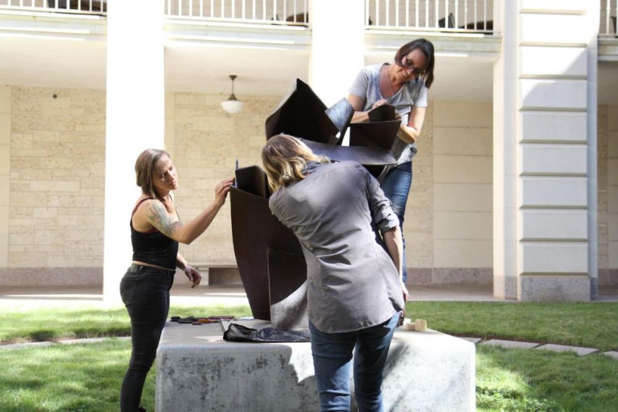 LPG volunteer Lisa Oppel (left) helps Katy Mckerley and Catherine Williams of Silver Lining Art Conservation apply protective oil to Willard Boepple’s sculpture Eleanor at 7:15 in the courtyard between Mezes and Batts halls.