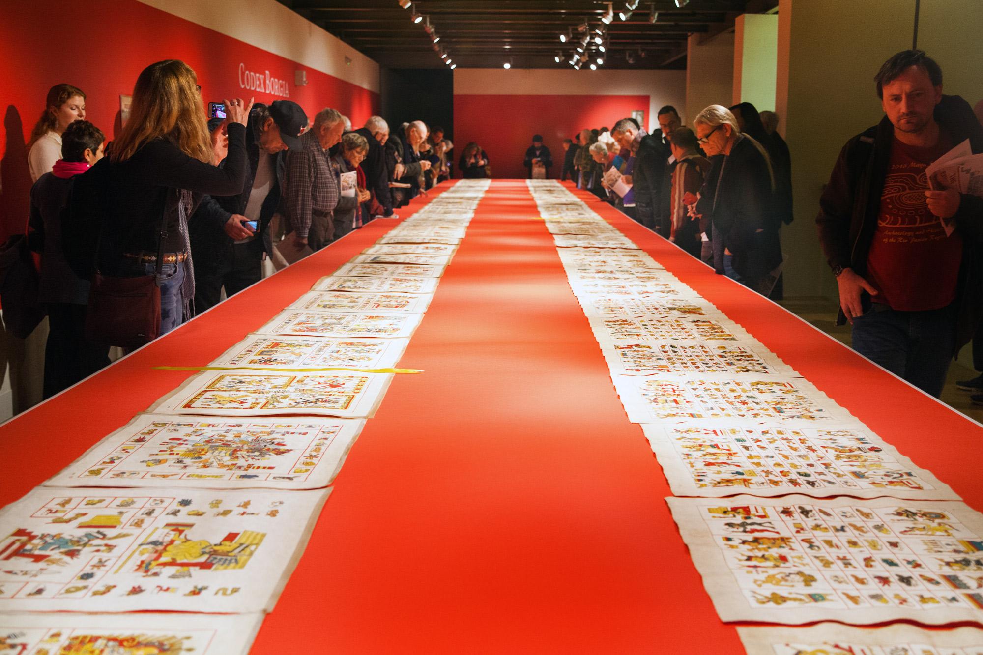People gather in an art gallery to view hand-painted squares of paper that replicate the Codex Borgia