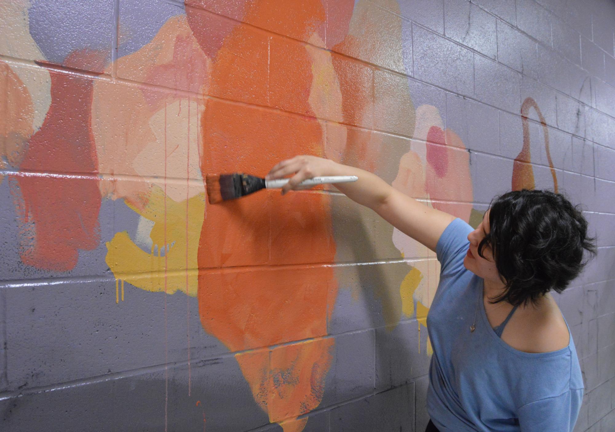 Victoria paints a mural on a wall in the Butler School of Music