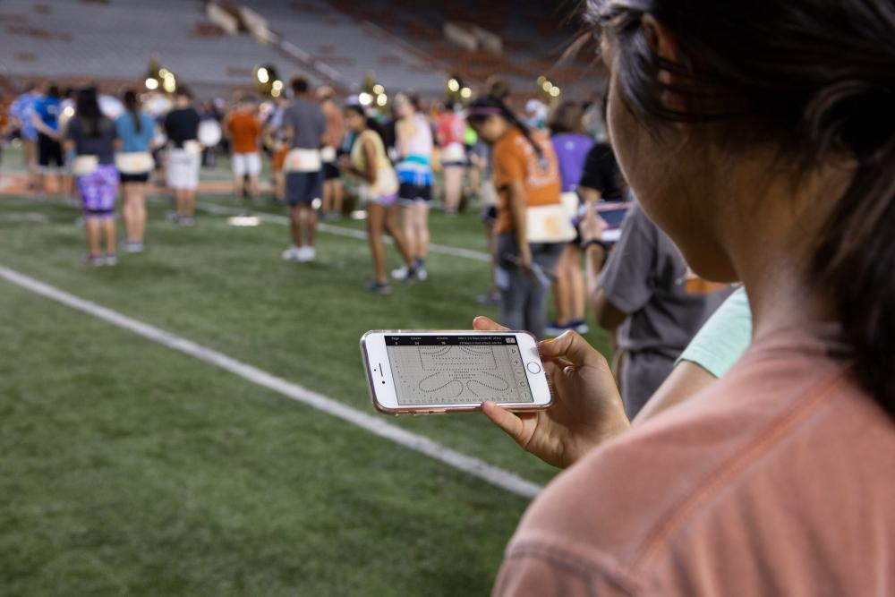 A UT Longhorn band member checks her phone for drill instructions