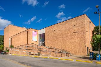 An exterior photo of a large brick building with Art Building on the front and a poster advertising a gallery space above the ramp and stairs.
