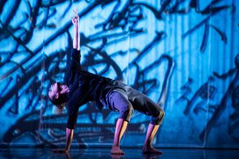 A dancer does a backbend on a stage in front of animated projection