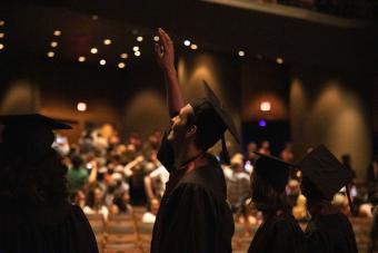 A student in a cap and gown waves at his family while walking into Bass Concert Hall for the College of Fine Arts commencement ceremony.