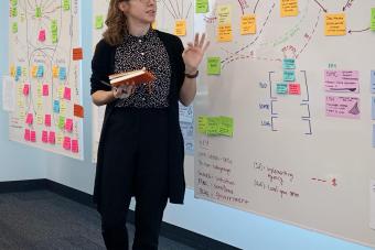 A woman stands in front of a white board full of Post-Its