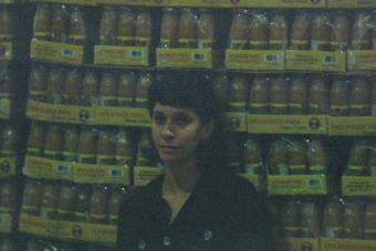 A grainy film portrait of an artist standing in front of crates of Topo Chico