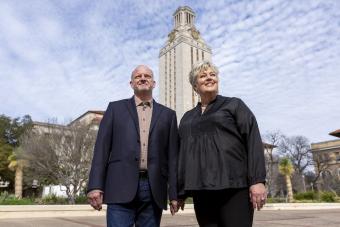 A couple stands in front of the UT Tower, gazing up at the blue sky.