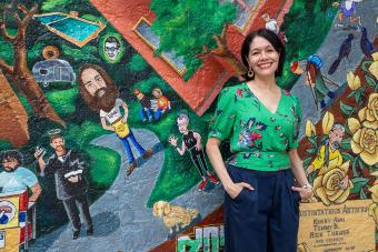 A woman in a green shirt smiles in front of a colorful mural