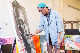 A student in a backwards cap paints a large portrait in an Art Building studio