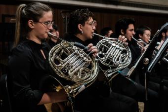 Students play french horn in an orchestra on a stage