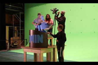 students maneuver a robot puppet in front of a green screen