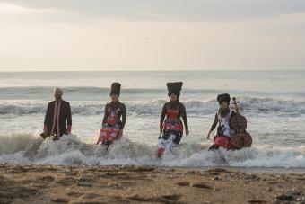 Four musicians emerge from the waves onto the sand with their instruments