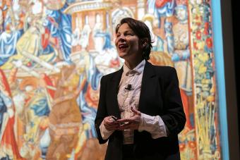 A speaker stands in front of a colorful background while addressing an audience
