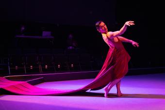 A male dancer in a red dress with long train on stage