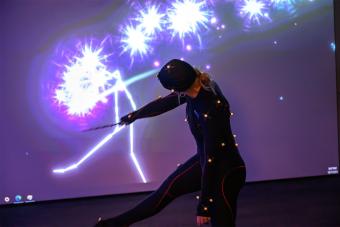 A dancer wearing motion sensors waves a wand to manipulate projection on a screen