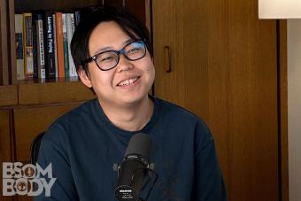 Yusong Zhao speaks into a mic with a bookshelf behind him.