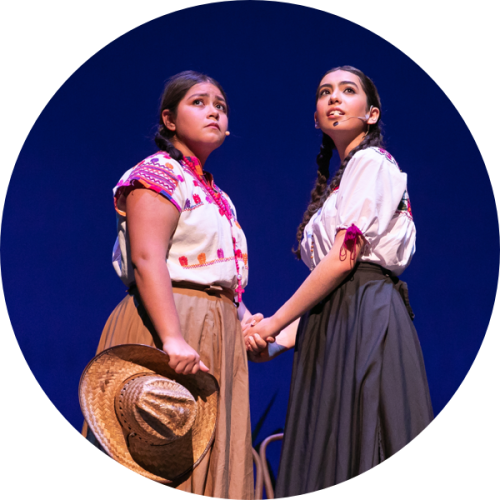 Two actresses in period costume clasp hands on stage.