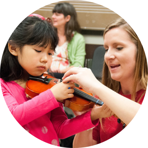 A UTeach Music student works with a young student on violin.