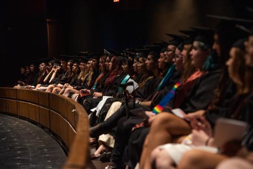 Students seated in rows wearing caps and gowns during a commencement ceremony.