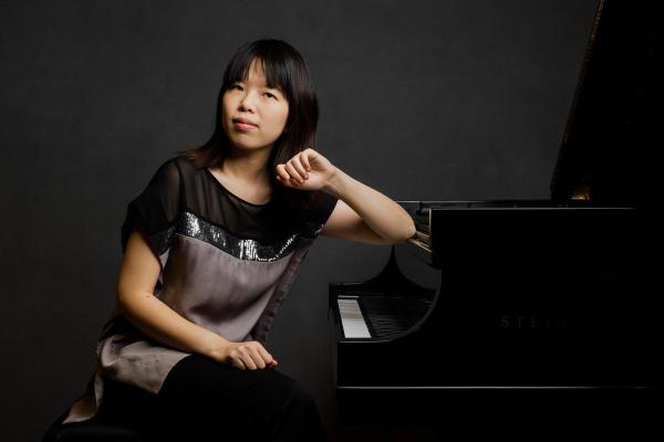 a female pianist sits at piano, looking at camera