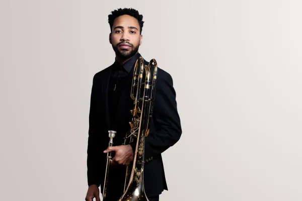A trombonist holding his trombone looks confidently into camera