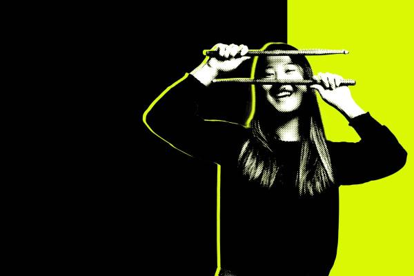 Black and white photo of a student holding drumsticks in front of a neon lime and black background.