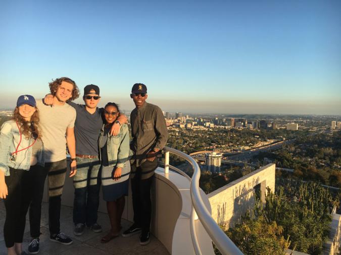 Five students pose on a balcony of the Getty Center with the Los Angeles skyline in the background