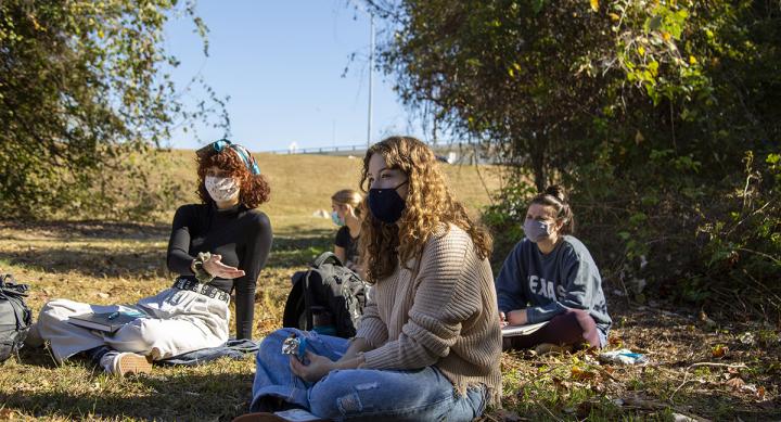 A group of masked students sit outside with their skechbooks