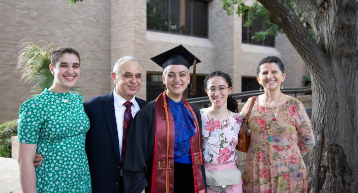 A family poses for a photo with a Fine Arts graduate in their cap and gown on the Bass Concert Hall plaza