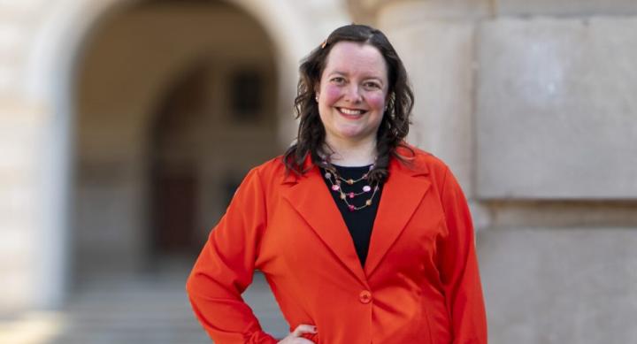 Course instructor Amira Pollock poses in a red blazer in front of an academic building.