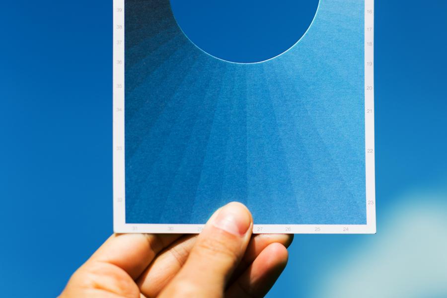 A hand holding a postcard against a blue sky. The postcard contains a spectrum of blue hues and has 