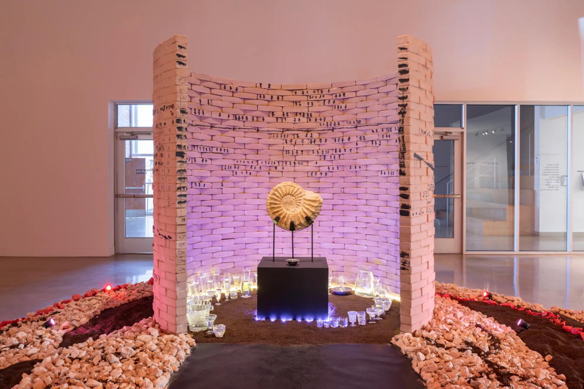An alter with a shell fossil is at the center of a semi-circle brick wall in a museum gallery space