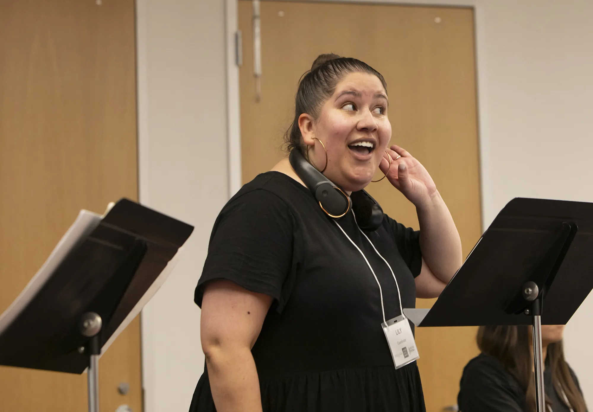 Lily Guerrero holds her hand up to her ear in "listen" gesture at a Meet the Opera program