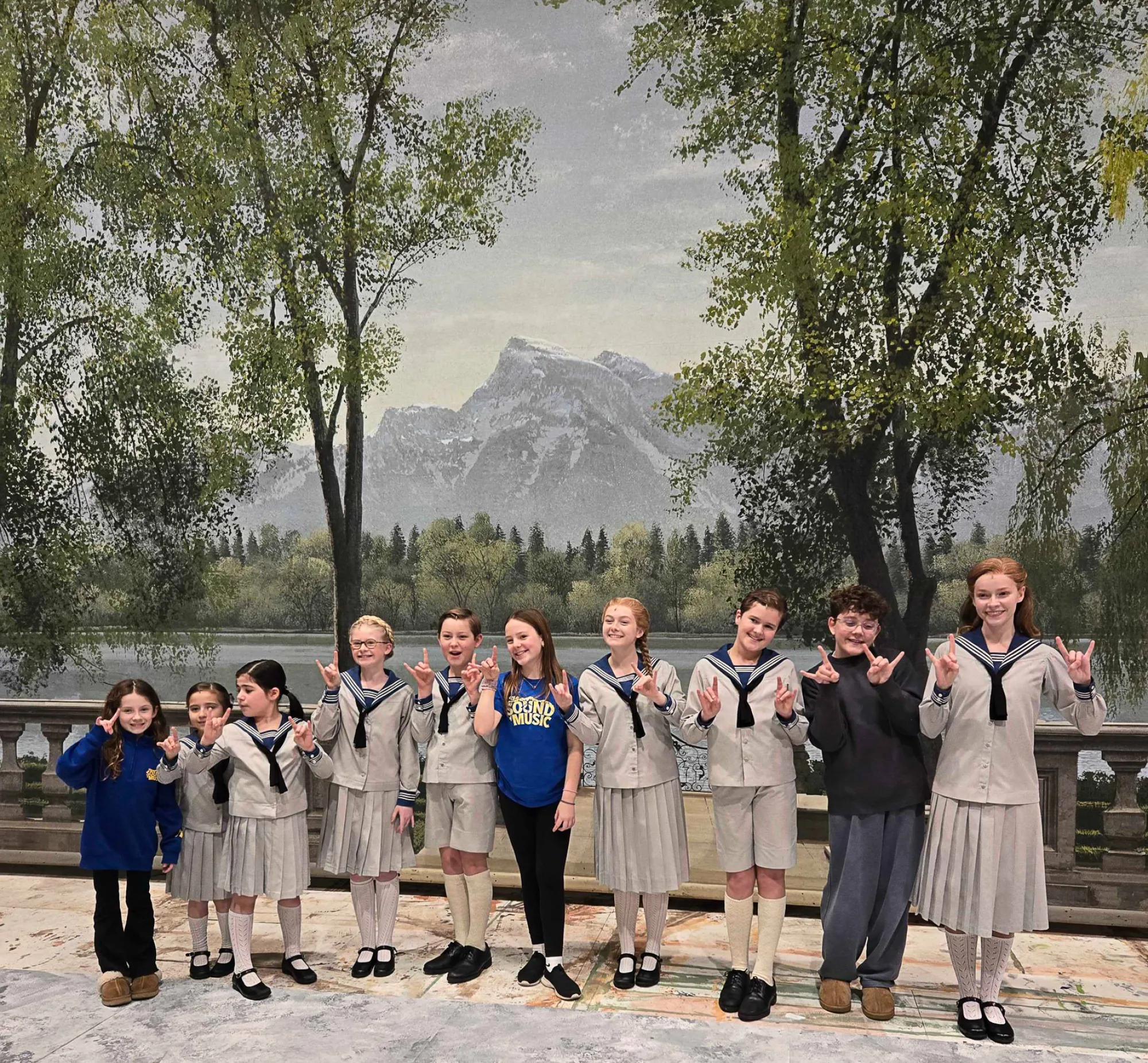 The cast of the touring production of The Sound of Music poses in front of the backdrop used in the film in Texas Performing Arts scenic shop.