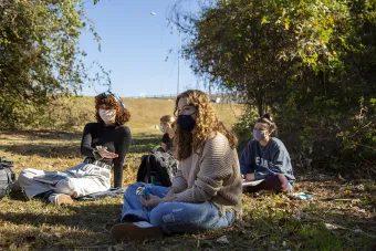 A group of masked students sit outside with their skechbooks