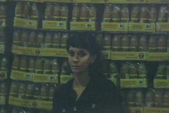 A grainy film portrait of an artist standing in front of crates of Topo Chico