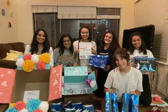 A group of six female college students pose with birthday party kits they created.